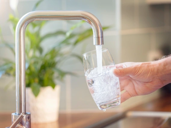 A person fills a drinking glass from a kitchen tap