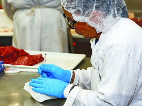 Woman in hairnet, gloves, and lab coat, writes on package