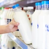 A customer chooses a bottle of milk from a well-stocked supermarket shelf