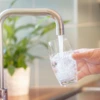 A person fills a drinking glass from a kitchen tap